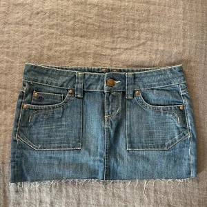 Lågmidjad jeanskjol - Säljer en snygg mörkblå jeanskjol från Esprit med fransig kant och låg midja. Kjolen har unika detaljer och en jättefin färg. Den sitter jätteskönt på mig som vanligtvis har M/38. Passar till nästan allt och perfekt till sommaren!