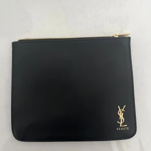 Svart YSL kuvertväska i skinn - Stilren svart kuvertväska från YSL med guldfärgad dragkedja och logga i hörnet. Som ny! Knappt använd. 