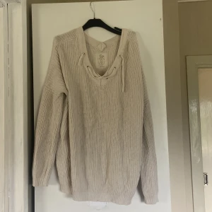 Beige stickad tröja med snörning Havana - Beige stickad tröja från Havana med v-ringning och snygg snörningsdetalj framtill. Tröjan har lång ärm, ribbade muddar och en avslappnad passform. Perfekt för lager-på-lager och chill höst- eller vinterstil. Har lite fläckar som säkert går bort i kemtvätt