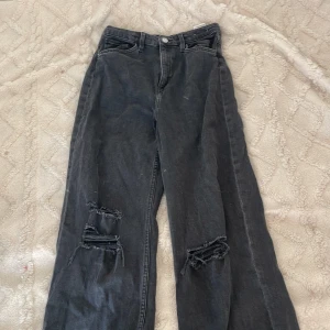 Svarta jeans. Baggy,highwaste. STORLEK: 170 barn/tjej - Säljer ett par svarta jeans från Pull&Bear med bred passform och snygga slitningar över knäna. Hög midja och klassisk femficksmodell. Jeansen har dragkedja och knapp framtill. Perfekta för en avslappnad och trendig look.