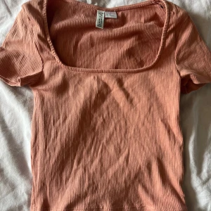 Ribbad persikofärgad topp H&M Divided XS - Superfin ribbad topp i persikofärg från H&M Divided. Modellen har urringning och korta ärmar. Mjuk och stretchig bomull som sitter snyggt och är perfekt till jeans eller kjol.