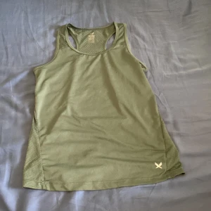 Olivgrön träningstopp från SOC - Sportig olivgrön linnetopp från SOC med brottarrygg och ventilerande meshpaneler på sidorna och ryggen. Tillverkad i lätt syntetmaterial som andas, perfekt för träning. Diskret logga framtill och stilren design.