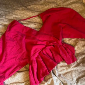 Röd omlottklänning med volang - Supersnygg röd omlottklänning med volangdetaljer nertill. Klänningen har smala axelband och är ärmlös, perfekt för dig som vill sticka ut. Materialet känns mjukt och stretchigt, vilket gör den bekväm att bära hela dagen.