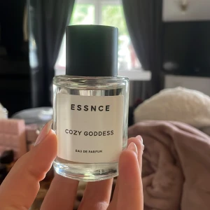 Essnce Cozy Goddess parfym - En stilren parfymflaska från Essnce med doften Cozy Goddess. Flaskan är genomskinlig med svart lock och vit etikett med minimalistisk text. Perfekt för dig som gillar enkla och snygga detaljer på parfymhyllan.