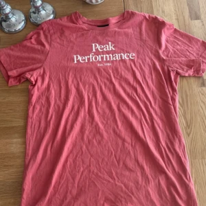 Rosa Peak Performance t-shirt - Snygg rosa t-shirt från Peak Performance med vit logga och text 'Est. 1986' på bröstet. Klassisk rund hals och korta ärmar. Skön och mjuk i bomull, perfekt till jeans eller shorts. Enkel och stilren design som funkar året runt.