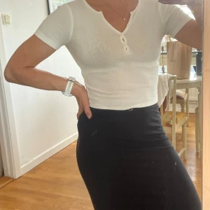 Vit ribbad topp från Gina Tricot - Supersnygg vit ribbad topp från Gina Tricot i croppad modell. Toppen har korta ärmar, v-ringning med dekorativa knappar framtill och sitter tight. Perfekt till jeans eller kjol för en fräsch look.