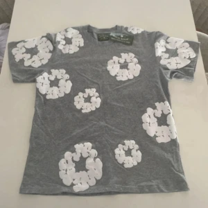 Denim tears - Snygg grå t-shirt från Soulland med stora vita blommiga mönster över hela tröjan. Klassisk passform och rund halsringning, perfekt för dig som vill sticka ut lite extra. Skön och mjuk bomullskvalitet.