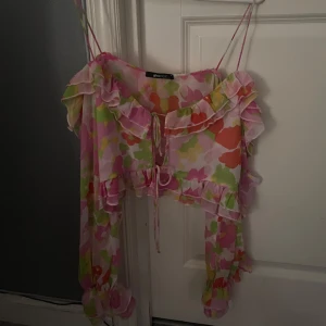 Blommig volangblus från Gina Tricot - Supersöt blommig blus från Gina Tricot med volanger och knyt fram. Topp i tunnt, luftigt material med långa ärmar och smala axelband. Färgerna är rosa, grön, orange och vit – perfekt för en färgglad look.