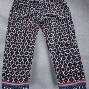 Mönstrade blå byxor med elastisk midja - Snygga byxor med elastisk midja från ZARA med tva sidfickor och färgstarkt mönster i blått, vitt och rött. Byxorna har ett unikt grafiskt mönster längs benen och en kontrasterande bård längst ner. Perfekta för dig som gillar statement-plagg och bekväm passform.