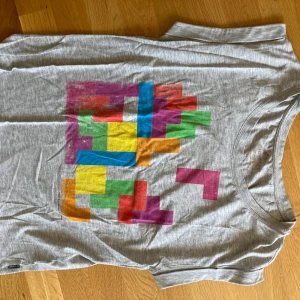 Grå t-shirt med Tetris-motiv - Säljer en grå t-shirt från ONLY med färgglatt Tetris-motiv på bröstet. T-shirten har rund halsringning och korta ärmar. Perfekt för dig som gillar retrospel och vill sticka ut med en lekfull stil.
