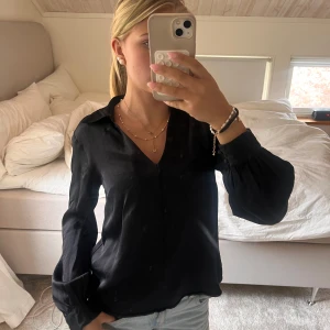 Svart blus med v-ringning - Svart blus med v ringning och lite puff ärm. Saknas en knapp på vänstra handleden. Men knappt använd.