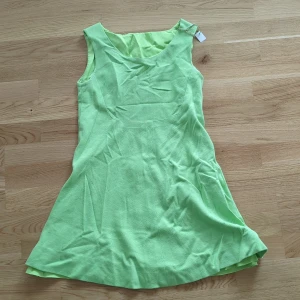 Vintage ljusgrön ärmlös kortklänning - Snygg ljusgrön 60tals kortklänning med ärmlös design och rund halsringning. Klänningen har ett slätt foder på insidan och är sydd i ett lätt, vävt tyg som ger en skön känsla. Sömmen på fodret har ett hål i ryggen, se bild. 