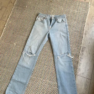 Ljusblå raka jeans - Säljer ett par ljusblå jeans med raka ben och snygga slitningar över knäna. Klassisk femficksmodell med normal passform och hög midja. 