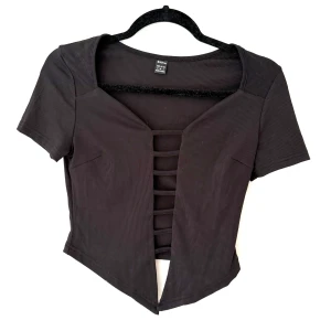 Svart croppad topp  - Svart croppad topp med ribbad struktur och coola banddetaljer framtill. Toppen har korta ärmar och en edgy öppen front med flera horisontella band. 