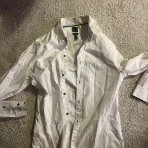 Vit skjorta från Kenneth Cole - Säljer en stilren vit skjorta från Kenneth Cole. Skjortan har långa ärmar och knappar framtill. Perfekt för en klassisk look.