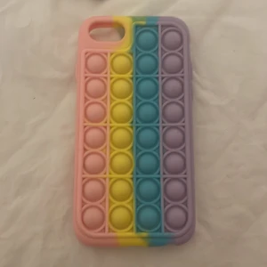 Färgglatt mobilskal med pop it-design - Säljer ett färgglatt mobilskal med pop it-design i rosa, gul, blå och lila. Skalet är både roligt och praktiskt, perfekt för att hålla mobilen skyddad och samtidigt ha något att pilla på. Passar till iPhone.