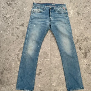 Blå jeans från Replay - Snygga blå jeans från Replay med en klassisk femficksdesign och lätt slitna detaljer. De har en rak passform och knappar i gylfen. Perfekta för en avslappnad stil.