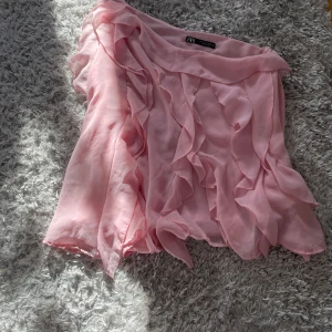 Rosa oneshoulder blus från Zara - Säljer en söt rosa oneshoulder blus från Zara med volangdetaljer. Perfekt för en somrig look. Blusen har en luftig passform och är tillverkad i ett lätt material. Storlek M
