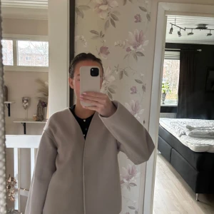 Beige kappa från Kappahl - Säljer en stilren beige kappa från Kappahl. Jackan har en enkel design med en knapp framtill och långa ärmar. Perfekt för en elegant look. Den är helt ny och aldrig använda 