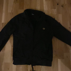 Svart jacka från Fred Perry -  Helt ny går för 2700krSäljer en stilren svart jacka från Fred Perry med dragkedja och det ikoniska logotypbroderiet på bröstet. Jackan har långa ärmar och en klassisk passform. Perfekt för en casual look. Jackan är S och Xs