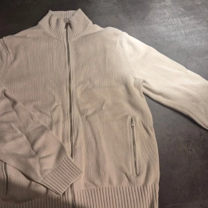 Vit stickad tröja från MNG - Säljer en stilren vit stickad tröja från MNG med dragkedja framtill. Tröjan har en hög ribbad krage och långa ärmar. Perfekt för kyligare dagar.