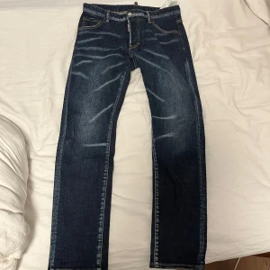 Mörkblå jeans från Dsquared2 - Snygga mörkblå jeans från Dsquared2 med knappgylf och kontrastsömmar. Tillverkade i Italien, dessa jeans har en klassisk design med en modern twist. Perfekta för dig som vill ha stil och kvalitet i ett. Pris sänks vid snabbaffär.