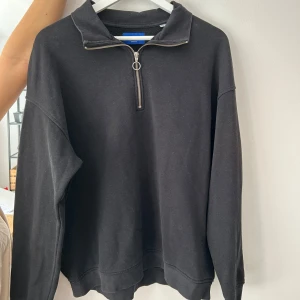Svart tröja med dragkedja från Jack & Jones - Säljer en svart tröja från Jack & Jones med dragkedja och hög krage. Perfekt för en avslappnad stil. Tröjan har långa ärmar och en enkel design som passar till det mesta. Lite urtvättad, annars inga defekter