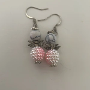 Örhängen med pärlor och stendetaljer - Charmiga örhängen med vita och rosa pärlor samt stendetaljer. De har en unik design med små metallvingar som ger en extra touch. Perfekta för att lägga till lite elegans i din stil.