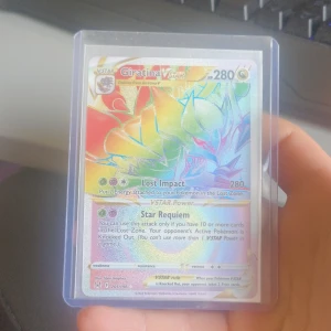 Giratina VSTAR Pokémonkort - Säljer ett Giratina VSTAR Pokémonkort med regnbågsglans. Kortet har 280 HP och inkluderar attackerna Lost Impact och Star Requiem. Perfekt för samlare eller spelare som vill förstärka sin kortlek med en kraftfull VSTAR-kort.