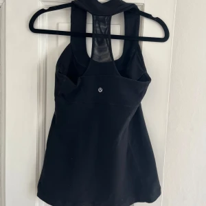 Svart linnetopp från Lululemon - Snygg och sportig svart linnetopp från Lululemon med brottarrygg.  Har inbyggd bh. 