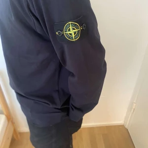 Svart Stone Island tröja  - Säljer en stilren svart tröja från Stone Island med deras ikoniska märke på ärmen. Tröjan har långa ärmar och en rund halsringning. Perfekt för en casual look. Storlek M men sitter som en L då den är stor i storleken.
