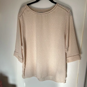 Beige prickig blus från Scotch & Soda - Säljer en elegant beige blus från Scotch & Soda med små svarta prickar. Blusen har trekvartsärmar och en avslappnad passform. Perfekt för en stilren look. 🌟