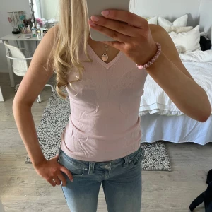 Ljusrosa ärmlös topp - Säljer en söt ljusrosa ärmlös topp med v-ringning. Perfekt för varma dagar och kan enkelt matchas med jeans eller kjol. Toppen har en enkel och stilren design.