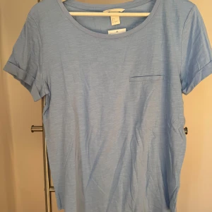 Ny, oanvänd, ljusblå T-shirt från H&M! - Ny, oanvänd, ljusblå T-shirt från H&M basic i storlek S med prislappen kvar. T-shirten har en fejk ficka på ena bröstet och ett tunt och mjuk tyg, perfekt inför en varm sommar.
