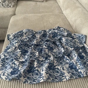 Blommig kjol i blått och vitt - Charmig kortkjol med volanger i ett vackert blommigt mönster i blått och vitt. Perfekt för en somrig look!