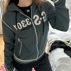 Zip up från G-Star - Säljer en mörkgrön zip up Hoodie från G-Star Raw med tryck på framsidan. Tröjan har långa ärmar och ribbade muddar med vita ränder. Vet ej om det är dam eller herr modell. 