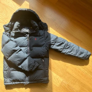 Polo Ralph Lauren marinblå dunjacka - Säljer en snygg marinblå dunjacka från Polo  Ralph Lauren med en klassisk röd broderad logga på bröstet. Jackan har en dragkedja framtill, praktiska fickor med dragkedjor samt en innerficka perfekt för värdesaker. Perfekt för kyliga dagar med sin vadderade design och huva, vattentät. Använd i 4 månader, från Johnells. Håller dig varm i -20°C. Skick 9/10👌Den mest populära jackan 2025 speciellt för ungdomar Nypris: 5495kr. Mitt pris: 3349kr Hör gärna av dig vid frågor. Priset är ej hugget i sten.