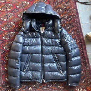Mörkblå dunjacka från Moncler - Säljer en snygg svart dunjacka från Moncler med huva och dragkedja. Jackan har långa ärmar och två praktiska fickor med dragkedja framtill. Perfekt för kyliga dagar! Skriv för mer bilder, köpt för ca 10 000 