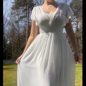 Vit långklänning med spetsdetaljer - Elegant vit långklänning med v-ringad omlott-design och spetsdetaljer på axlarna. Klänningen har korta ärmar och ett flödande kjolparti. Klänningen har endast testats och är i nyskick🥰 jättevacker och smickrande klänning som jag köpte från vila🙌🏻 orginalpris 900kr🙏 köparen står för frakt🙌🏻