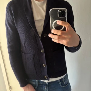 Mörkblå cardigan från Pier One - Säljer en stilren mörkblå cardigan från Pier One. Koftan har knappar framtill och är perfekt för en avslappnad look. Den är tillverkad i ett mjukt material och har långa ärmar.