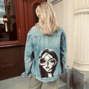 AMORA 003 - Jeansjacka från JAQUÍ med trycket AMORA 003 Ärmlängd (från armhåla): 53 cm Byst: 59 cm Längd: 66 cm Storlek: L Modellen är 167 cm lång.