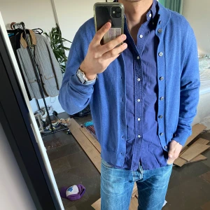 Blå kofta från Alan Paine - Säljer en stilren blå kofta från Alan Paine i lyxig bomull. Koftan har knappar framtill och ribbade muddar vid ärmslut och nederkant. 