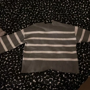 Grå och vit randig tröja från H&M - Säljer en stilren grå och vit randig tröja från H&M. Tröjan har långa ärmar och en ribbad nederkant samt ärmslut. Perfekt för en avslappnad look.