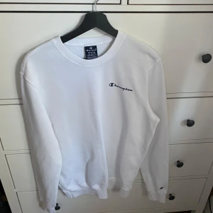 Vit sweatshirt från Champion - Säljer en klassisk vit sweatshirt från Champion med deras logga tryckt på bröstet. Tröjan har en rund halsringning och långa ärmar. Fungerar för både herr och dam i storlek M!