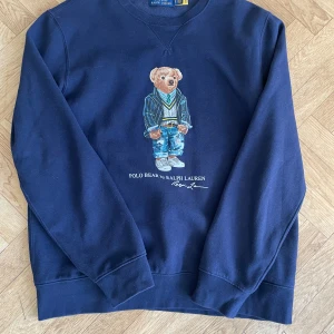 Mörkblå sweatshirt från Ralph Lauren - Säljer en snygg mörkblå sweatshirt från Ralph Lauren med en ikonisk Polo Bear-design på framsidan i bra skick. Tröjan har långa ärmar och en rund halsringning. 