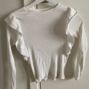 Vit ribbad tröja från med volanger - Säljer en söt vit ribbad tröja från Zara med volangdetaljer längs ärmarna. Tröjan har långa ärmar och en rund halsringning💗