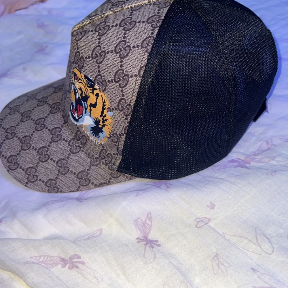 Snygg keps från Gucci med ett djärvt tigertryck framtill och det ikoniska GG-mönstret. Kepsen har en justerbar rem baktill i grönt och rött. Perfekt för att ge din outfit en lyxig touch. Helt oanvänd snabbaffär kvitto finns!. Asusteet.