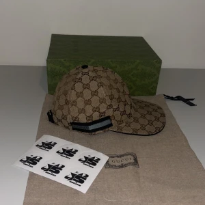 Beige keps från Gucci limited edition - Snygg beige keps från Gucci med det klassiska GG-mönstret. Kepsen har en justerbar rem baktill och en böjd skärm. Perfekt för att ge din outfit en lyxig touch. Finns i S & M
