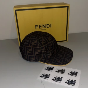 Mönstrad keps från Fendi - Snygg keps från Fendi med ett distinkt mönster i svart och brunt. Kepsen har en klassisk skärm och justerbar passform. Perfekt för att ge din outfit en lyxig touch.