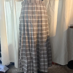 Rutig långkjol i beige och vit - Snygg långkjol med rutigt mönster i beige och vit. Kjolen har en klassisk och tidlös design med veckad stil som ger en elegant look. Perfekt för både vardag och speciella tillfällen. Behöva stryxkas men annars väldig fin, tjockt skönt material. Gjord i Danmark. 